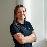 Employee in a black Carado polo shirt standing by the window with arms crossed