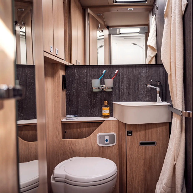 Baderom med dagslys med hylle, vask, håndkleholder, speil, klesstang og toalett i HYMER B-ML T