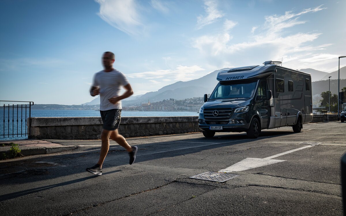 Løper forbi parkert HYMER MasterLine T ved kysten i Sør-Frankrike under blå himmel