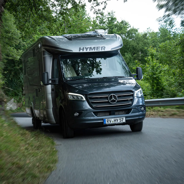 Kjører opp en vei omgitt av skog som går oppover HYMER MasterLine T på Mercedes-chassis