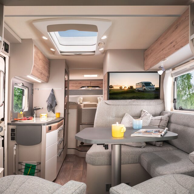 Living area in the HYMER Exsis-t 580 with seating area and plasma TV (showing a background image) as well as the entrance door, kitchen area and sleeping area