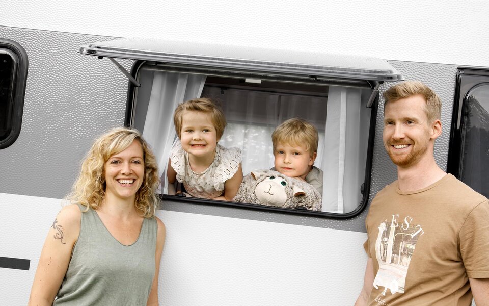 Op de foto is een stel te zien dat voor een LMC Sassino caravan staat terwijl twee kinderen door het open raam kijken.
